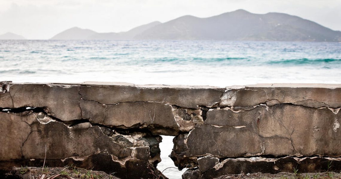 An old broken and cracked coastal wall sitting in front of the the ocean. Island mountains can be seen in the distance
