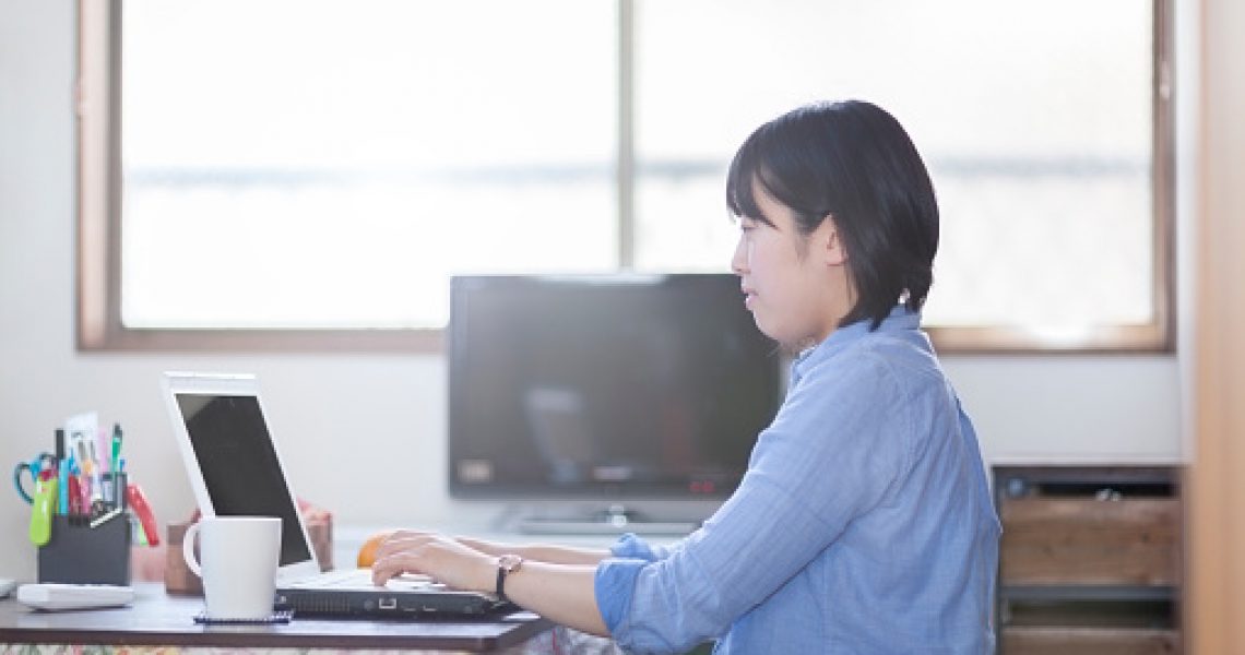 A young Japanese woman is doing her work on her laptop at her home-office.