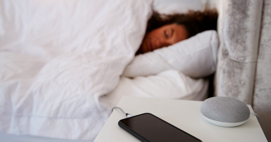 Woman Asleep In Bed With Mobile Phone And Voice Assistant On Bedside Table